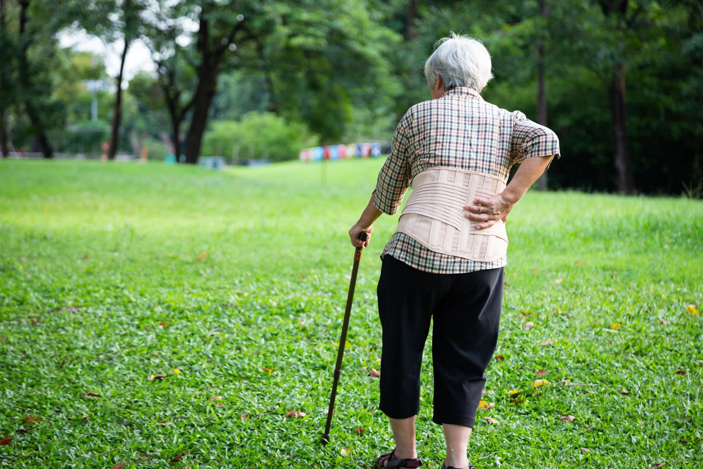 Senior woman walking in a park holding her hip and low back in pain, myofascial release for neck, back and hip pain when walking, Greenville SC, Organic Mechanics