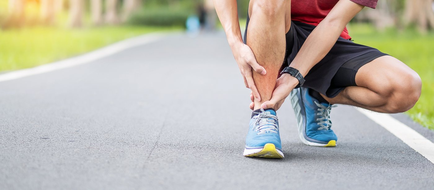 Runner stopped on the road holding his lower leg, shin and calf pain from running, neuromuscular therapy in Greenville SC